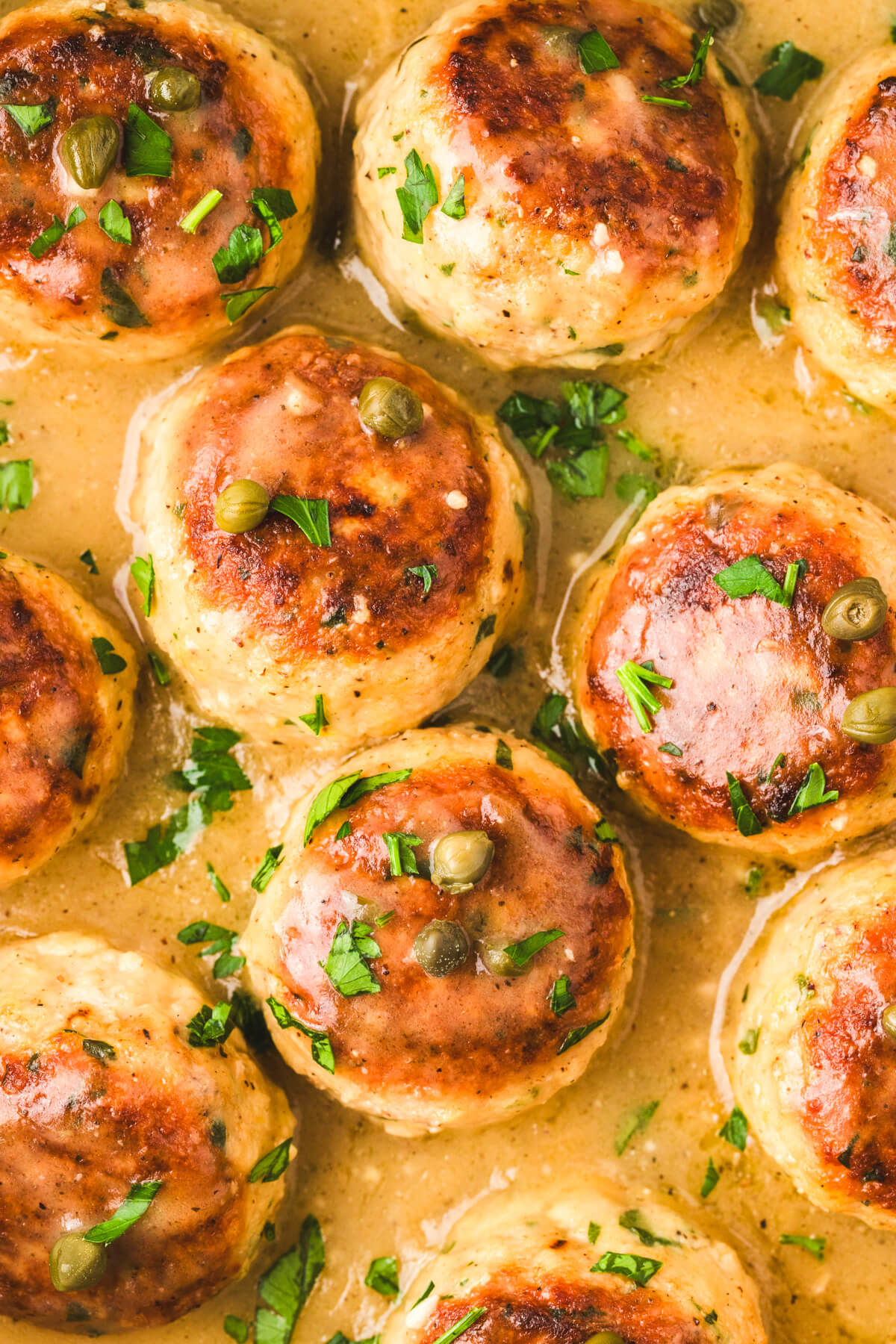 Close up photo of chicken piccata meatballs garnished with chopped Italian parsley. 