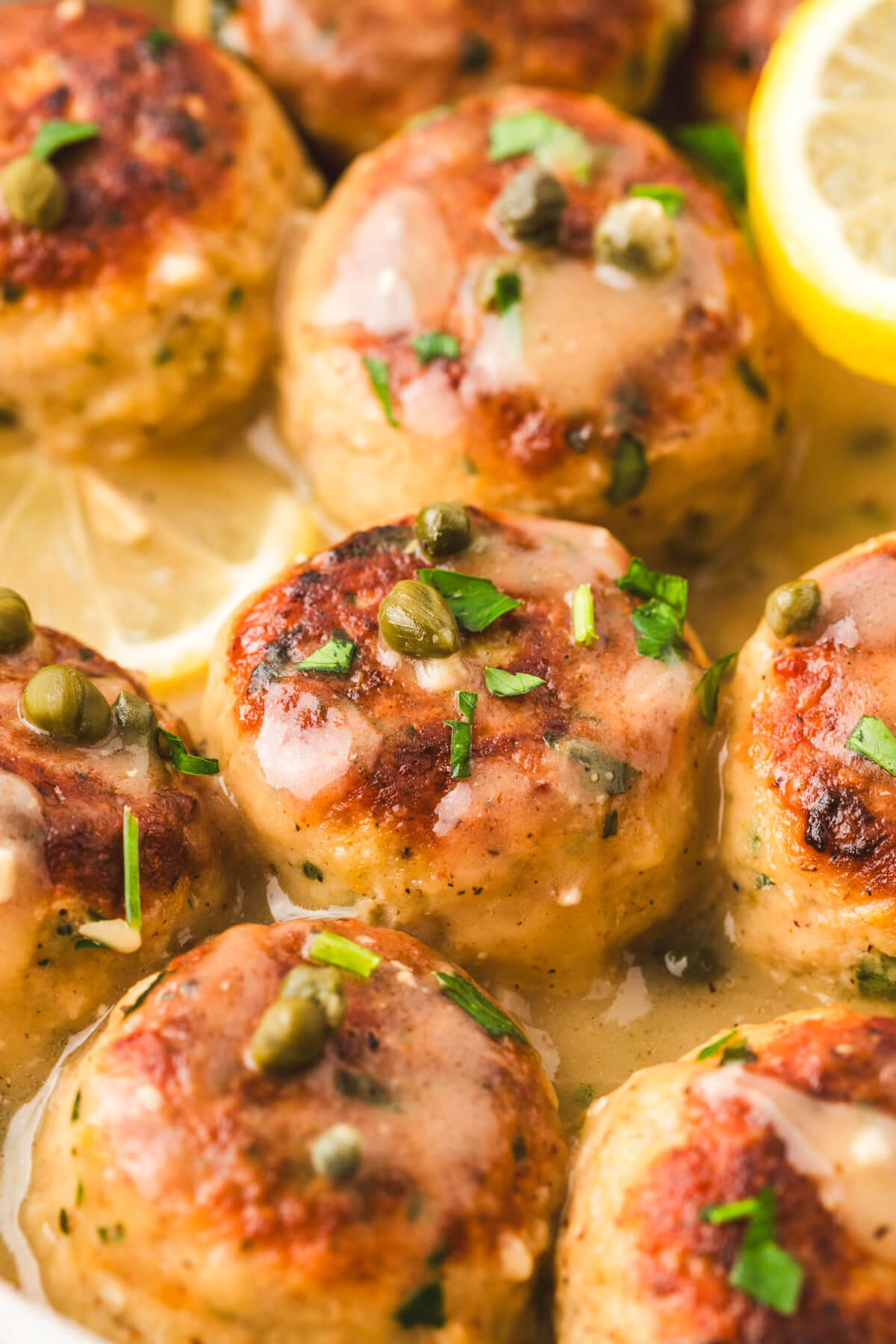 Close up photo of chicken piccata meatballs garnished with wedges of lemon and chopped Italian parsley.