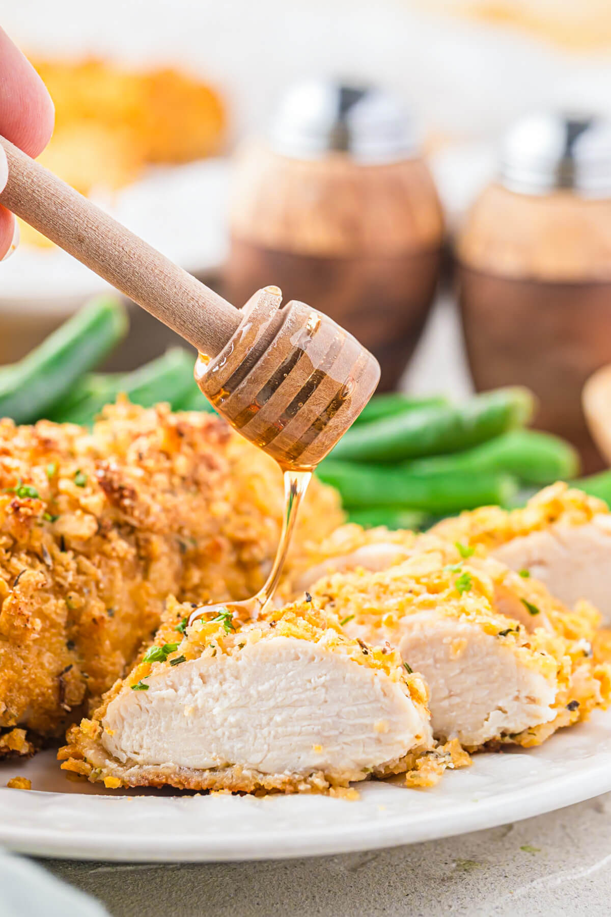 A honey wand drips honey over a golden baked cornflake chicken tender.