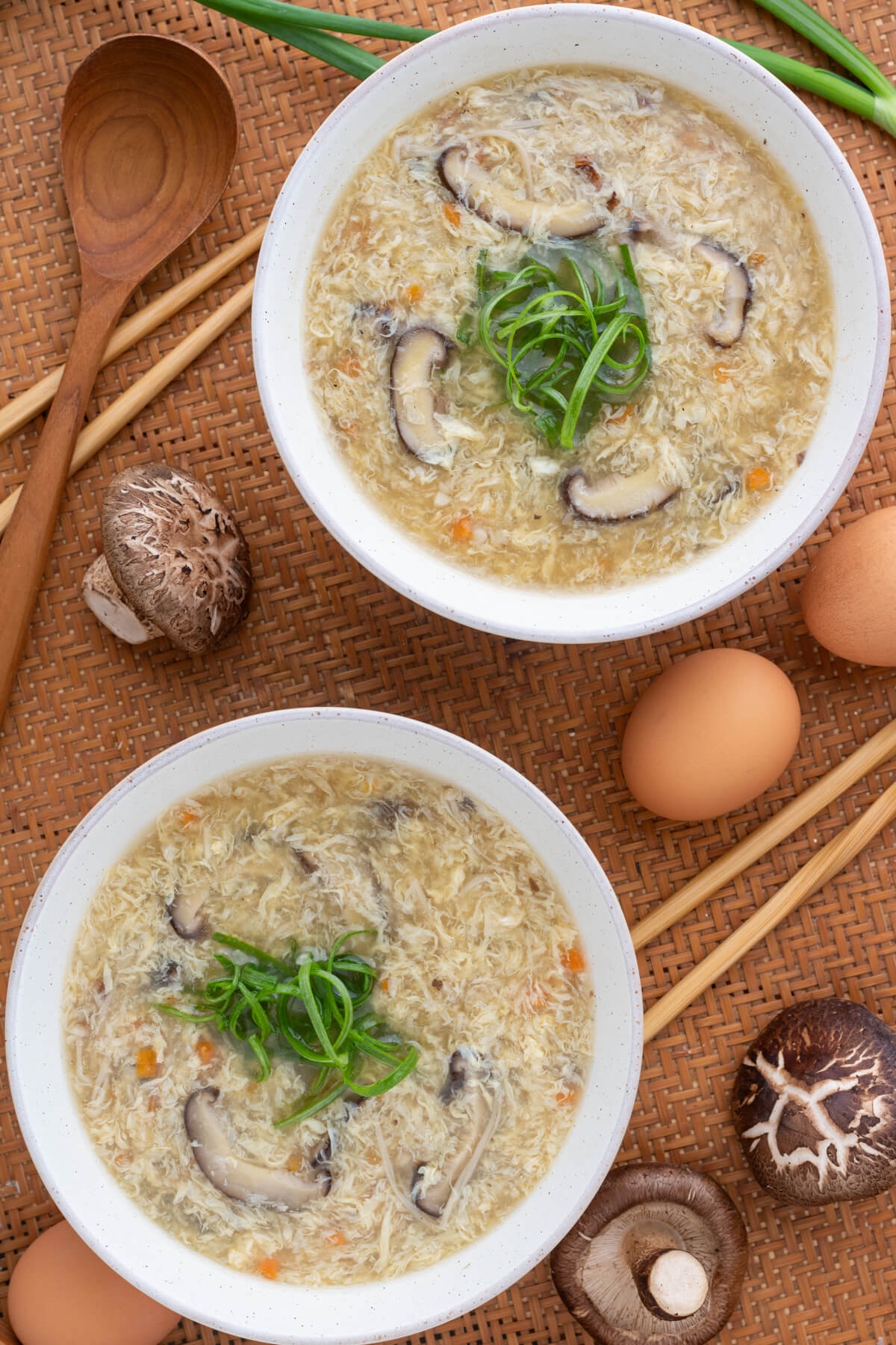 Two white bowls of Egg Drop Soup containing shiitake mushrooms and finely diced carrots garnished with shredded green onions.