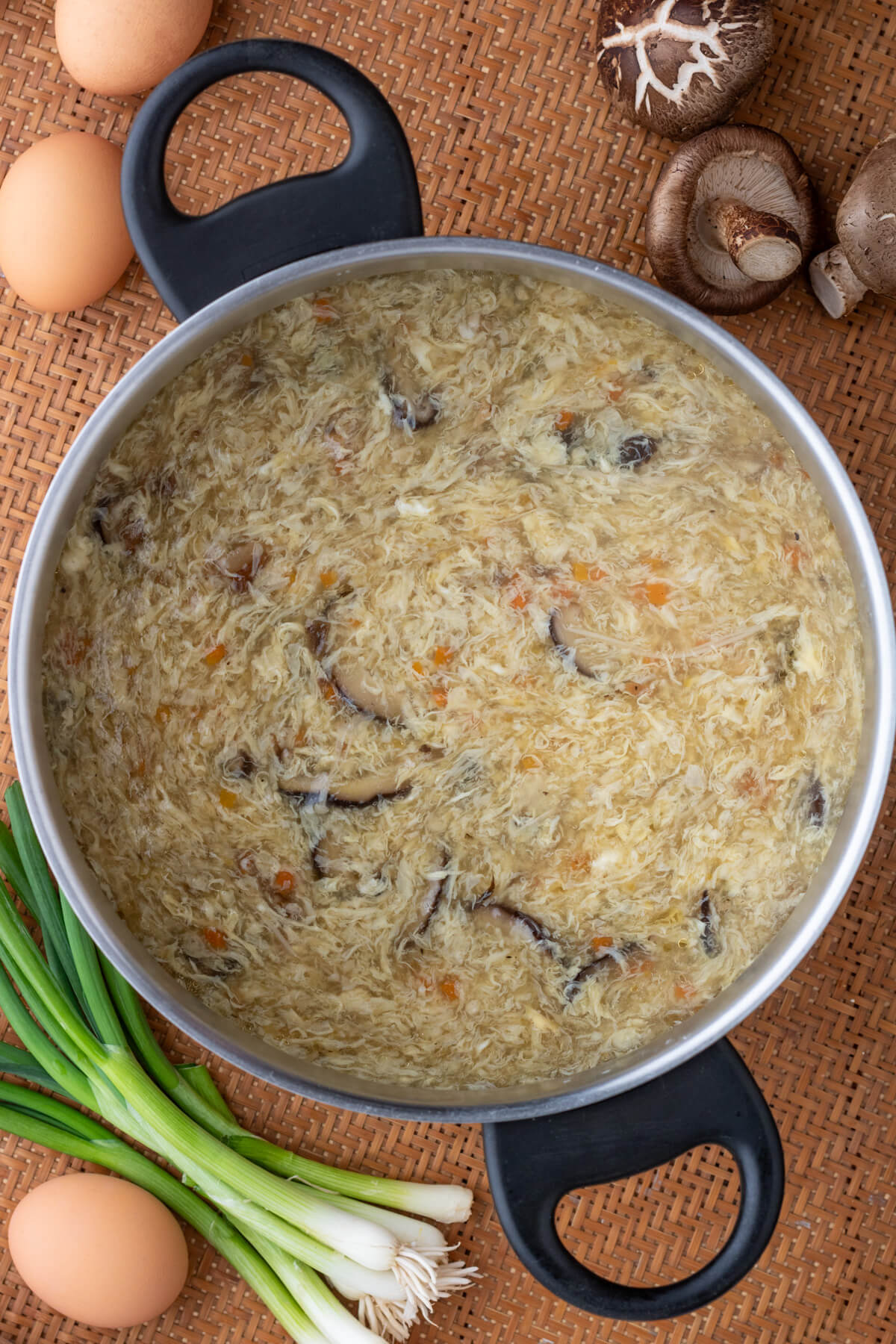 A soup pot full Egg Drop Soup containing shiitake mushrooms and finely diced carrots.