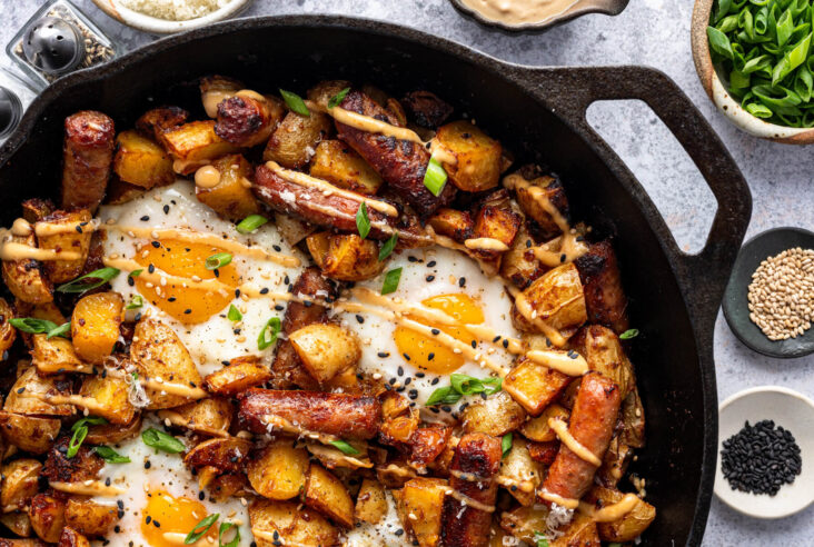 A baked breakfast skillet featuring eggs, potatoes, and breakfast sausage drizzled with maple miso sauce on a breakfast table.