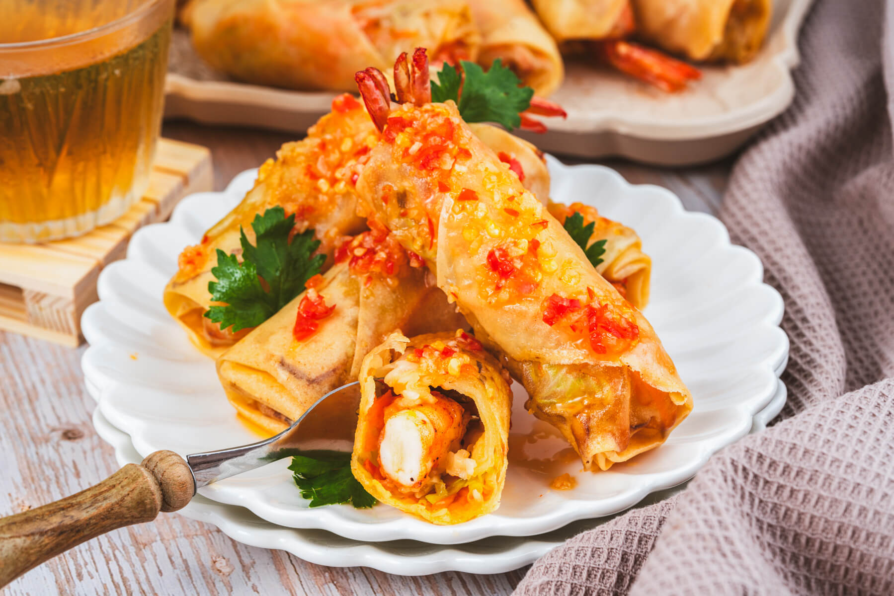 Golden fried shrimp spring rolls covered with bright Thai chili sauce on a white plate. 