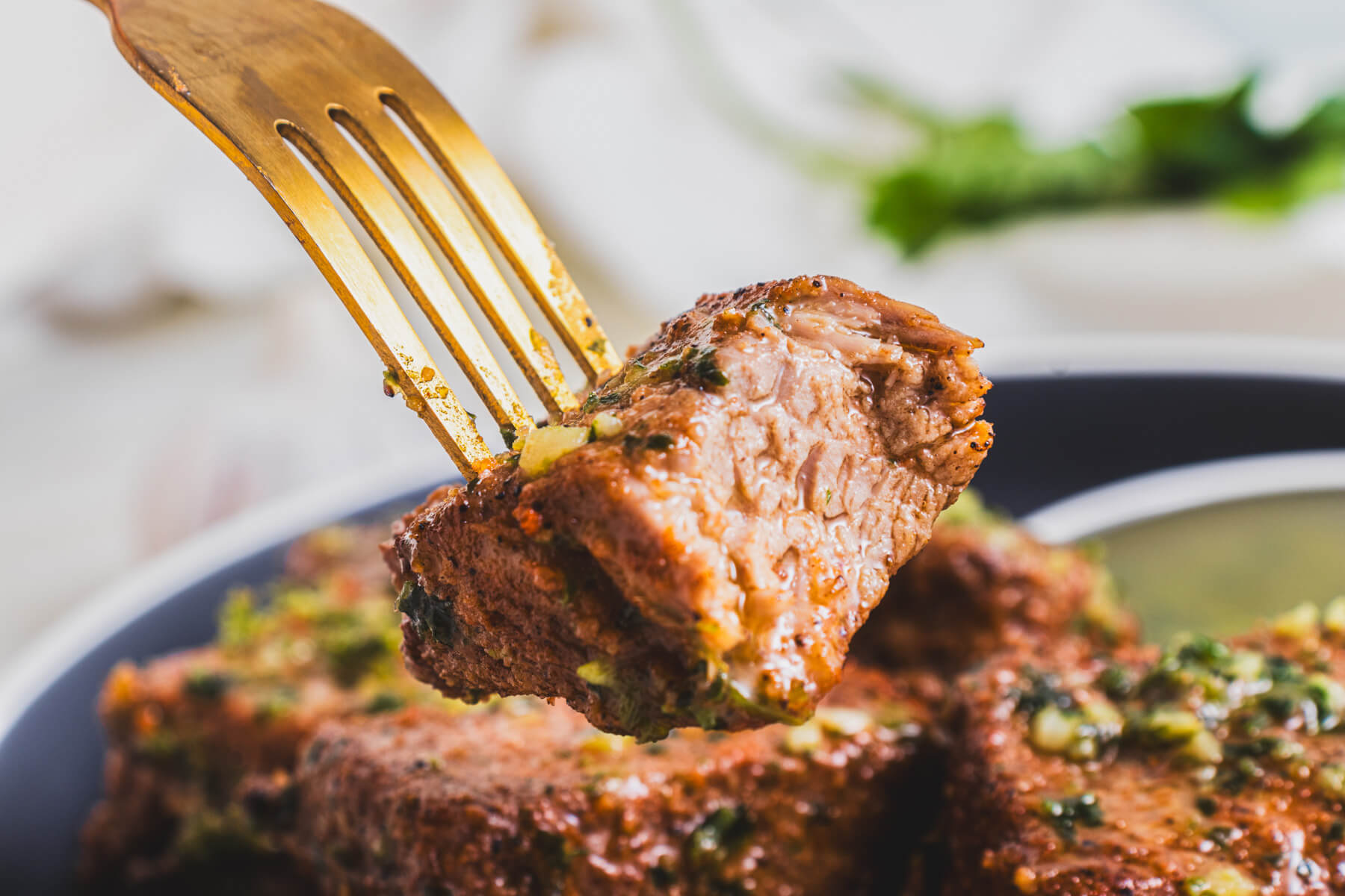 A fork holds a perfectly seared air fryer Steak Bite over a bowl of steak bites.