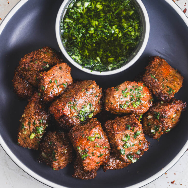 A low bowl full of perfectly seared air fryer steak bites topped with garlic parsley butter.