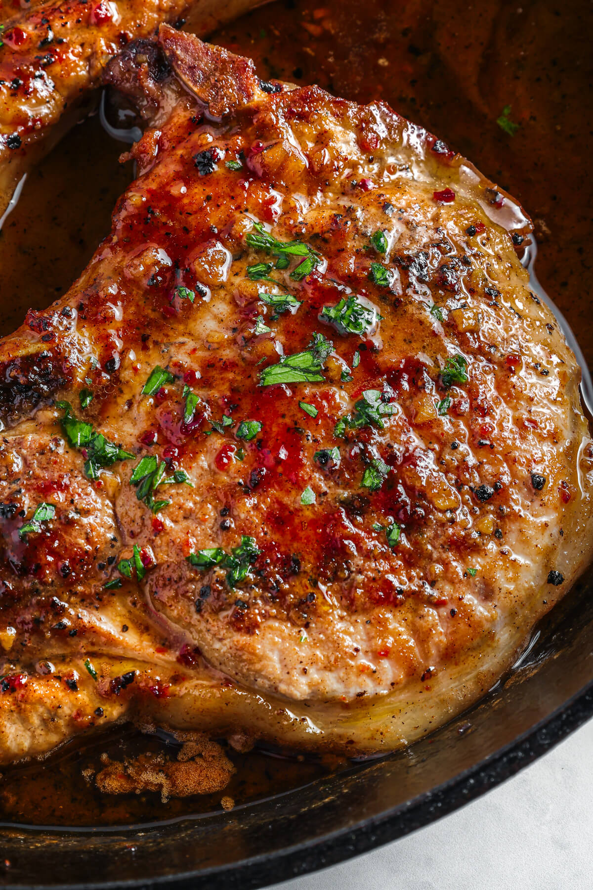 A perfectly seared brown sugar pork chop covered in luxurious brown sauce, parsley, and garlic in a cast iron skillet.