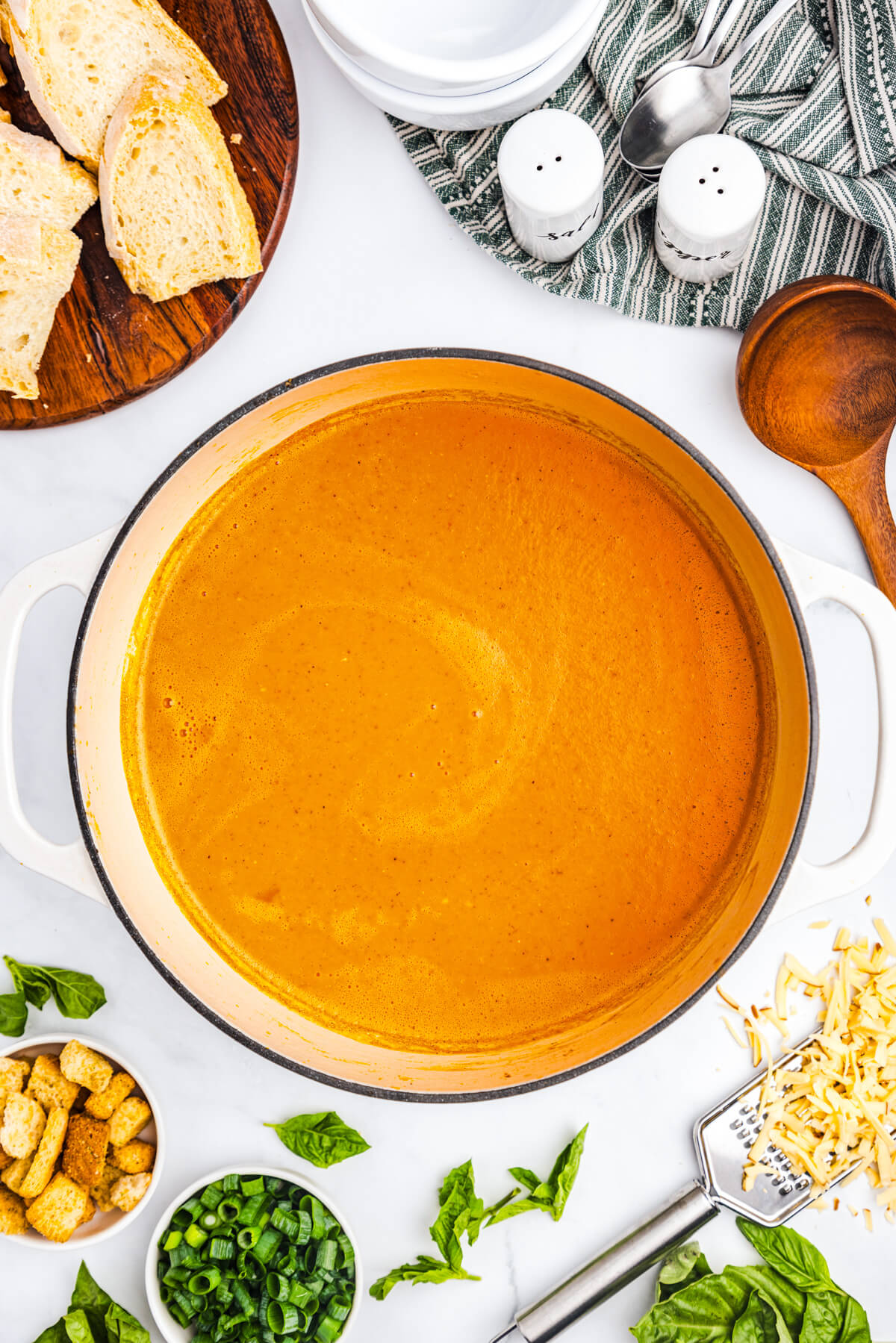 A soup pot full of bright orange, smooth and creamy Roasted Red Pepper Soup surrounded by ingredients and garnishes.