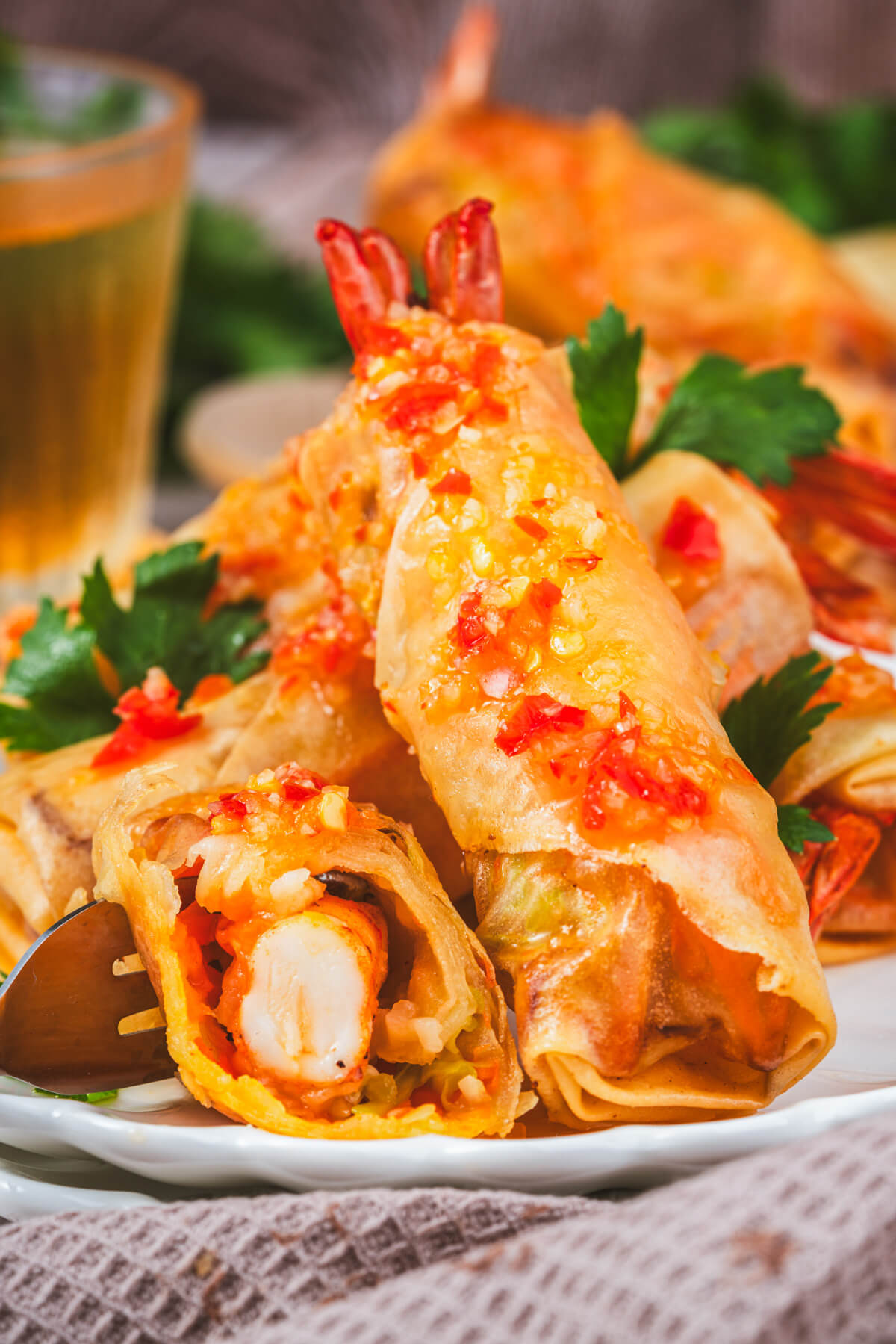 Golden fried shrimp spring rolls covered with bright Thai chili sauce on a white plate.