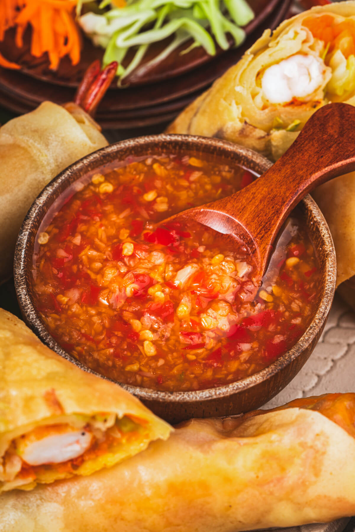 A bowl of bright Thai chili sauce nestled among golden fried shrimp spring rolls.