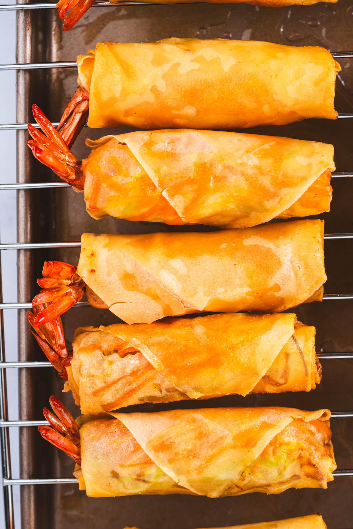 Five golden fried shrimp spring rolls on a wire rack.