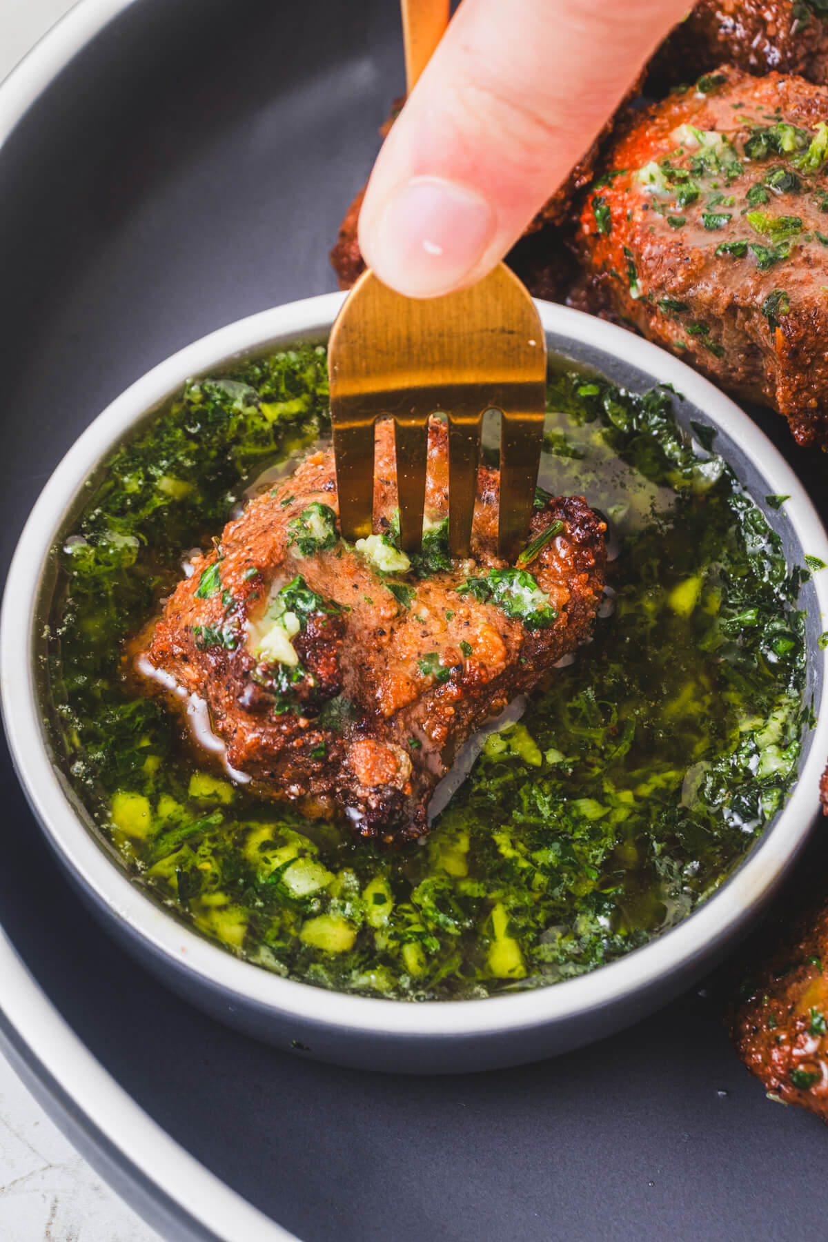 A fork dips an air fryer steak bite into a small bowl of garlic parsley butter sauce.
