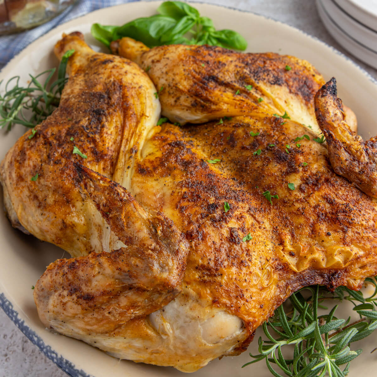 A crispy brown skinned whole roast spatchcock chicken on a platter garnished with fresh herbs on a dinner table.