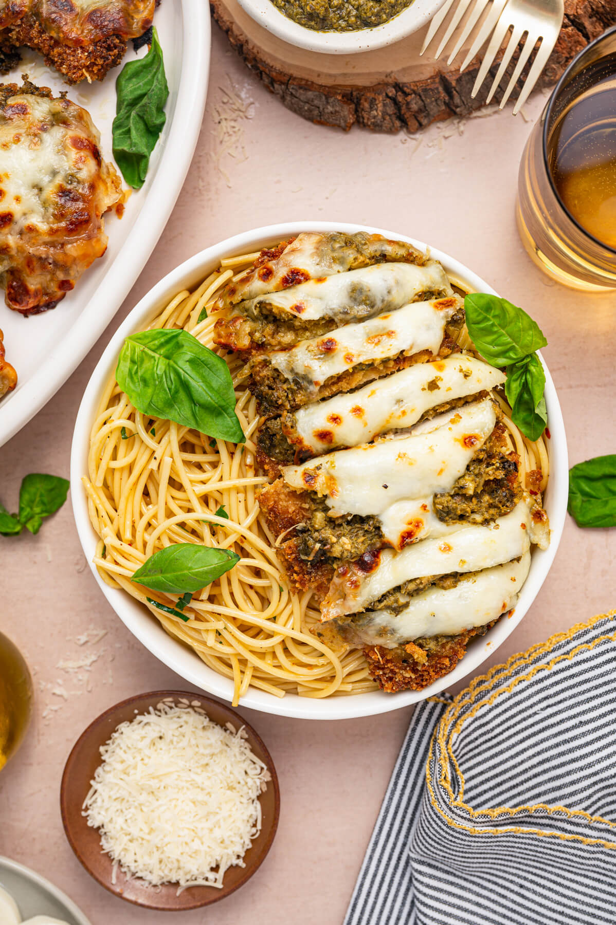 Baked and sliced Pesto Chicken Parmesan covered in green pesto, red tomato sauce, and gooey melted mozzarella cheese in a bowl of spaghetti.