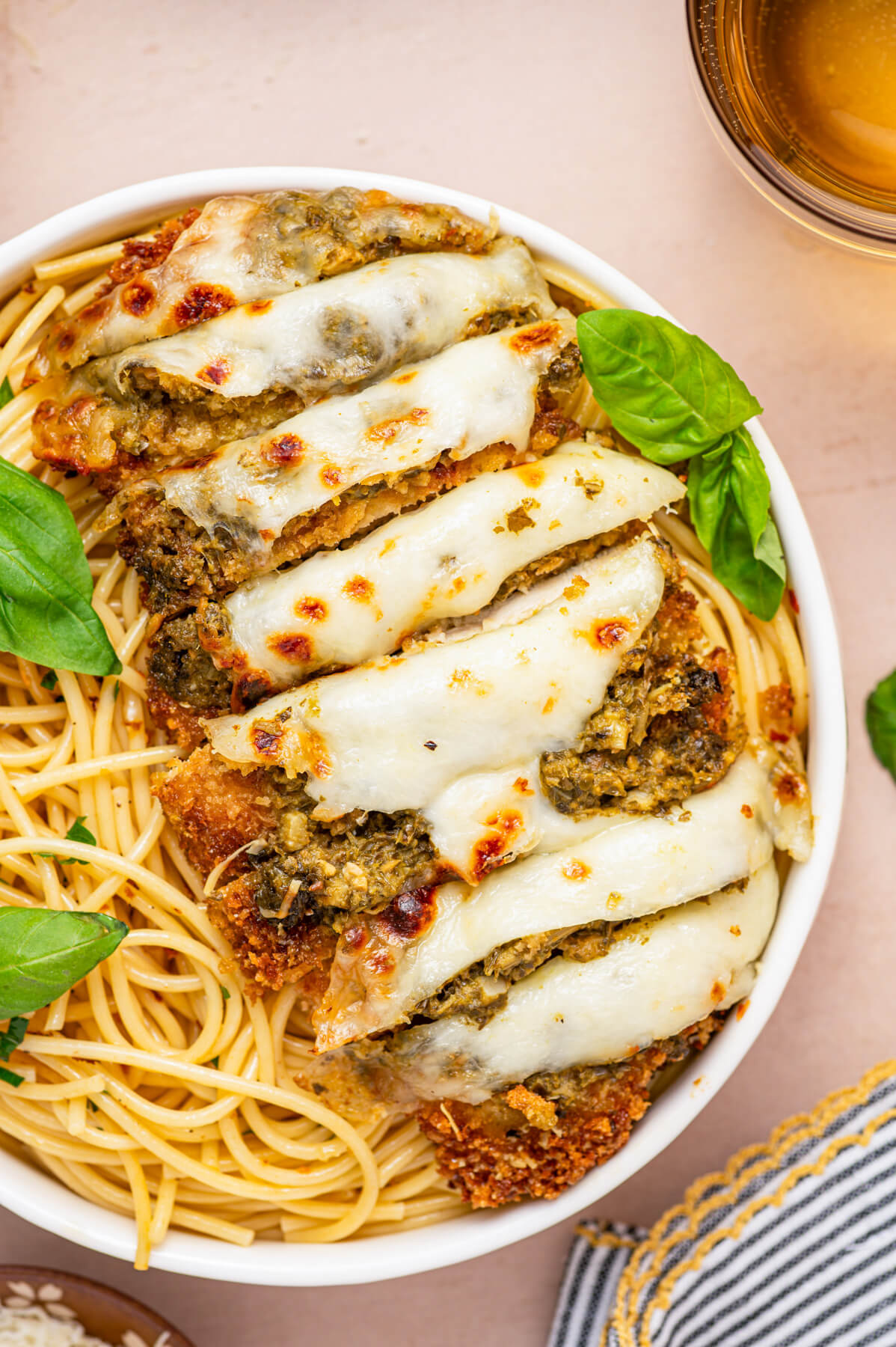 Baked and sliced Pesto Chicken Parmesan covered in green pesto, red tomato sauce, and gooey melted mozzarella cheese in a bowl of spaghetti.