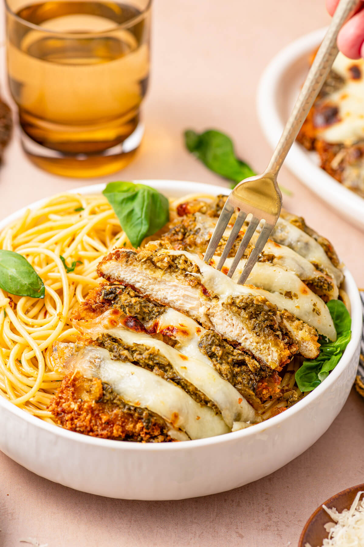 Baked and sliced Pesto Chicken Parmesan covered in green pesto, red tomato sauce, and gooey melted mozzarella cheese in a bowl of spaghetti.