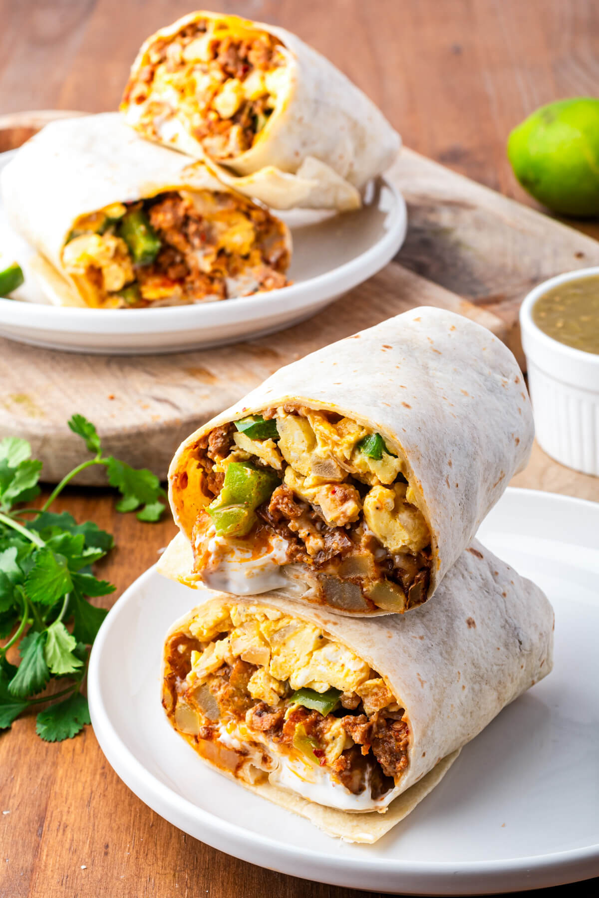 Two burritos on a white plate sliced open to show the spicy red chorizo, soft scrambled eggs, melted cheese and vegetables inside.