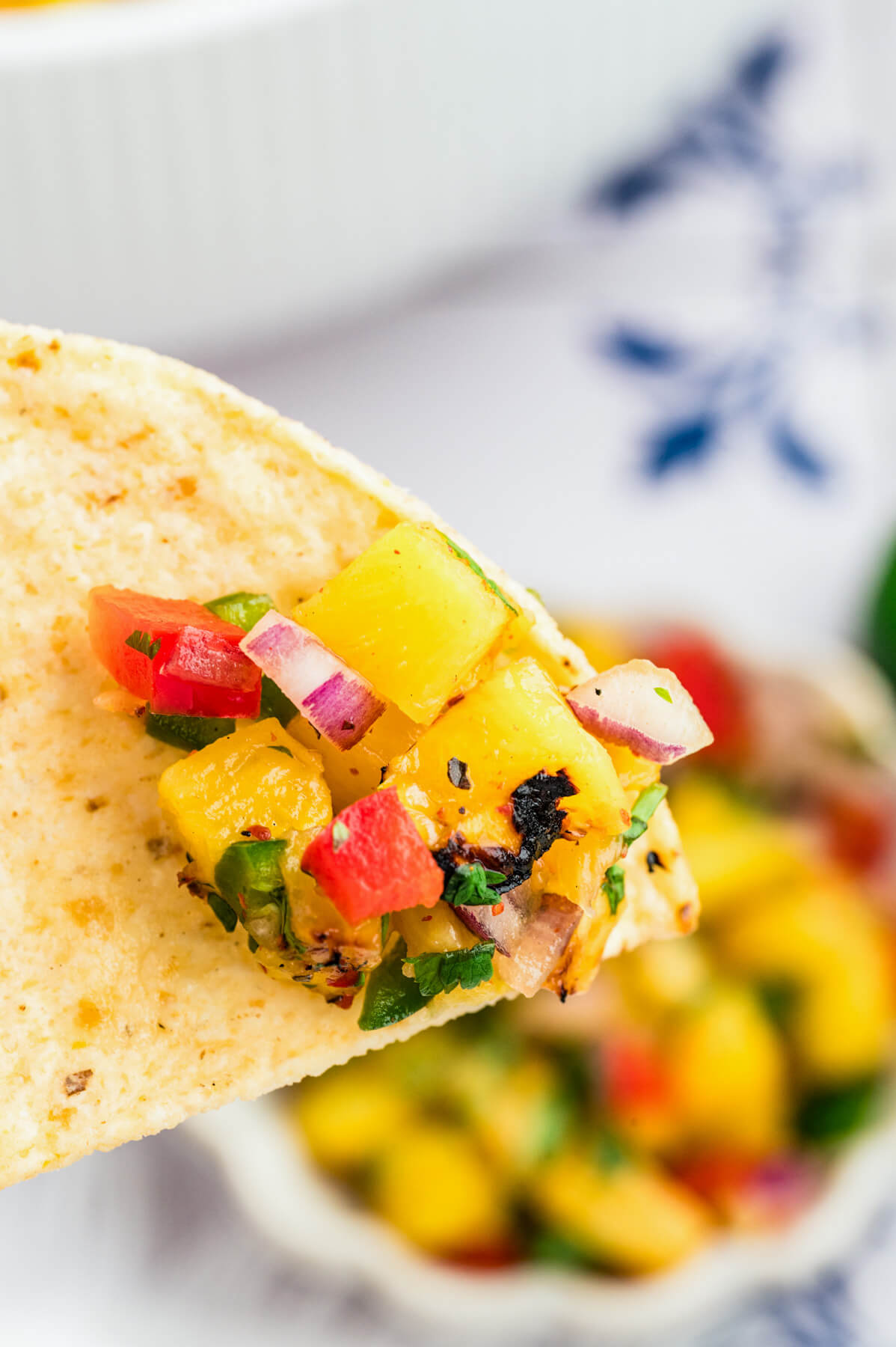 A tortilla chip containing a bite sized portion of grilled pineapple salsa.