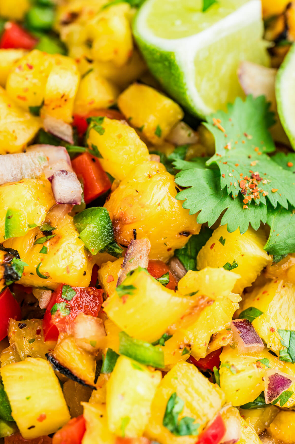 Close up image of grilled pineapple salsa featuring vibrant green cilantro, red bell peppers, red onions, and diced jalapenos.