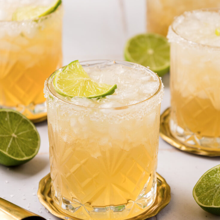 Three icy Mezcal margaritas in salt rimmed rocks glasses with lime garnishes.
