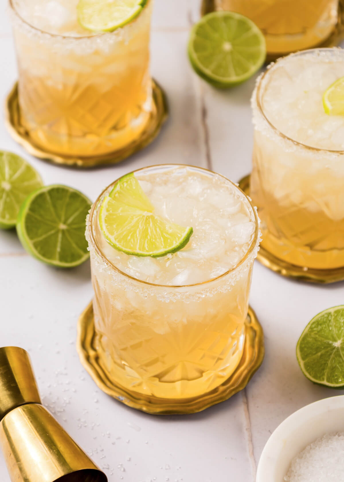 Three icy Mezcal margaritas in salt rimmed rocks glasses with lime garnishes.