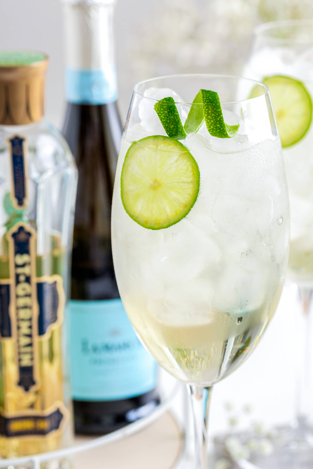An icy St. Germain Spritz cocktail in large wine glass garnished with a slice of lime.