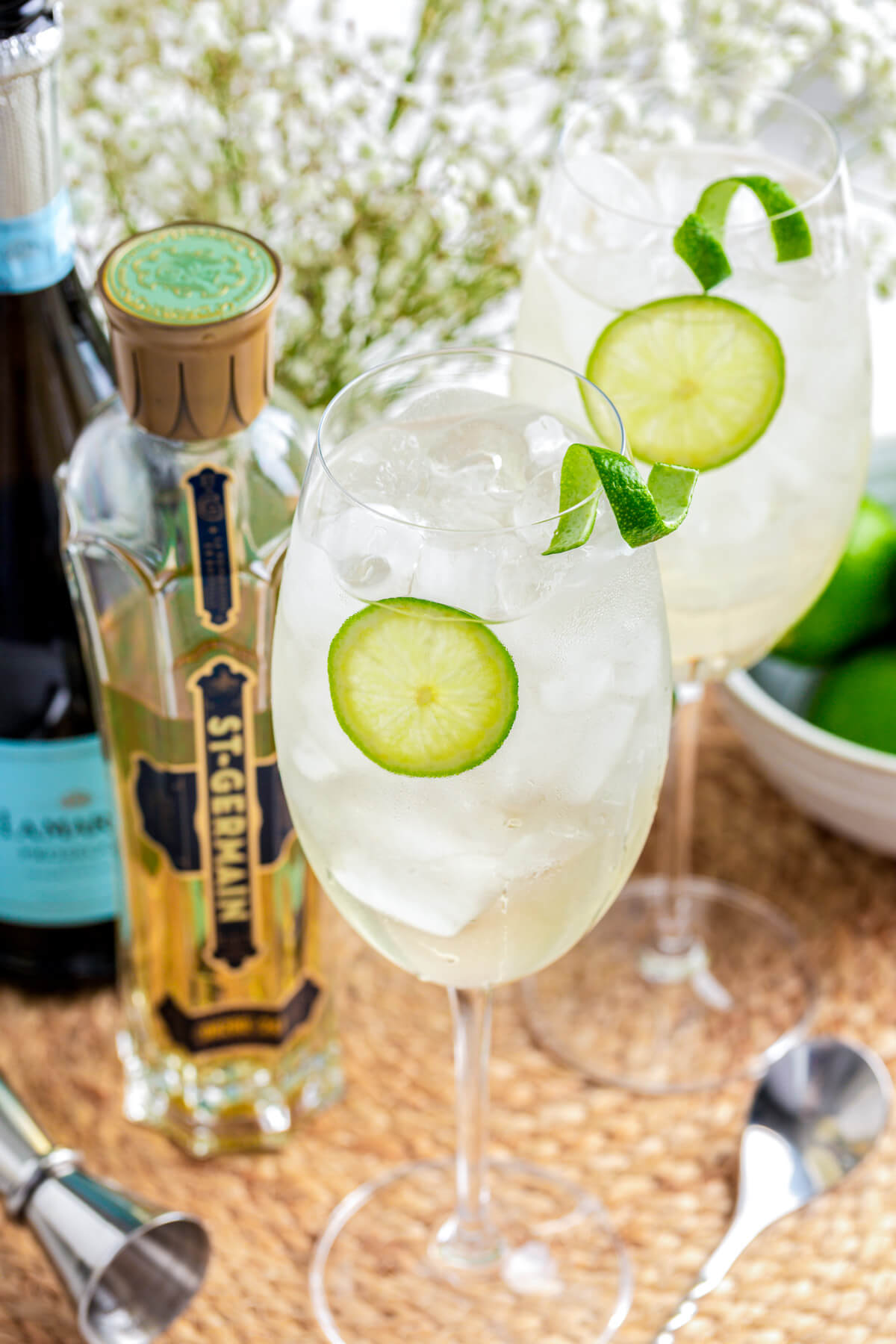 Two icy St. Germain Spritz cocktails in large wine glasses garnished with slices of lime.