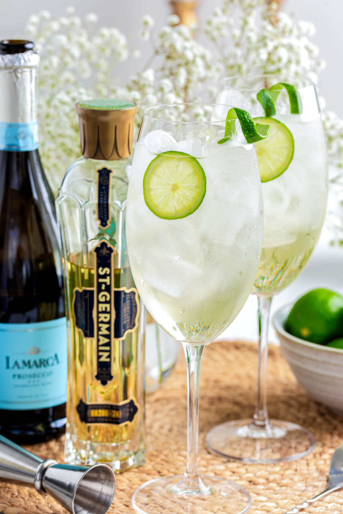 Two icy St. Germain Spritz cocktails in large wine glasses garnished with slices of lime.