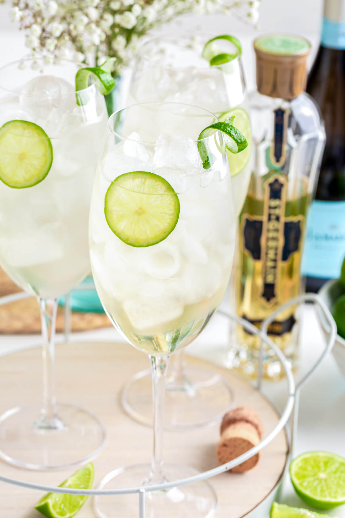 Three icy St. Germain Spritz cocktails in large wine glasses garnished with slices of lime.