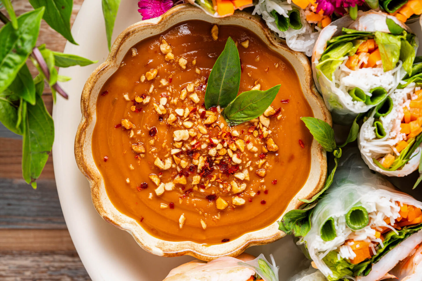 A small dish of Vietnamese peanut sauce garnished with chopped peanuts and red chili flakes surrounded by salad rolls.