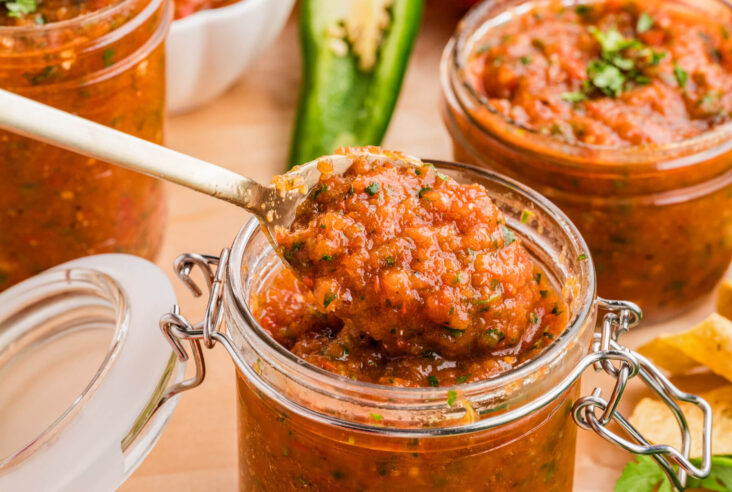 A spoon full of fire roasted salsa sits on top of a jar of the same salsa.