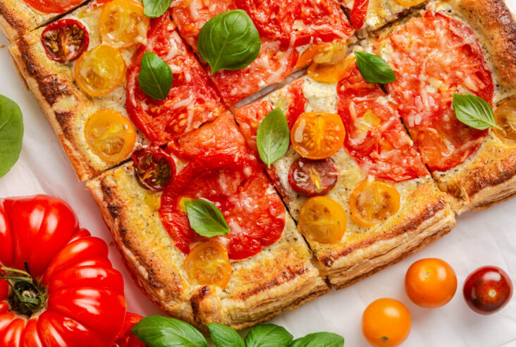 Brightly coloured slices of Heirloom tomato tart garnished with fresh basil leaves.
