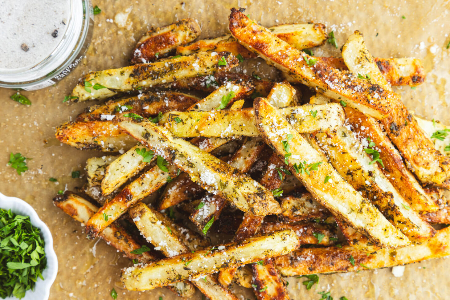 A group of golden brown oven baked truffle fries dotted with parsley and black truffle salt on butcher paper.