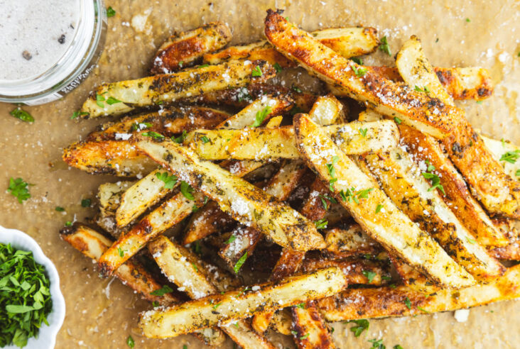 A group of golden brown oven baked truffle fries dotted with parsley and black truffle salt on butcher paper.