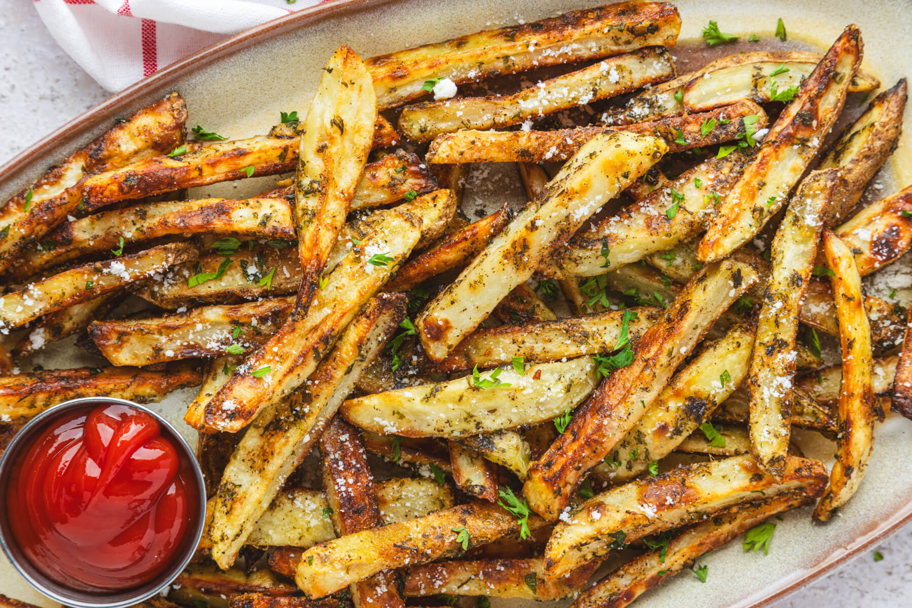 A plate of golden brown oven baked truffle fries dotted with parsley and black truffle salt with a container of ketchup.