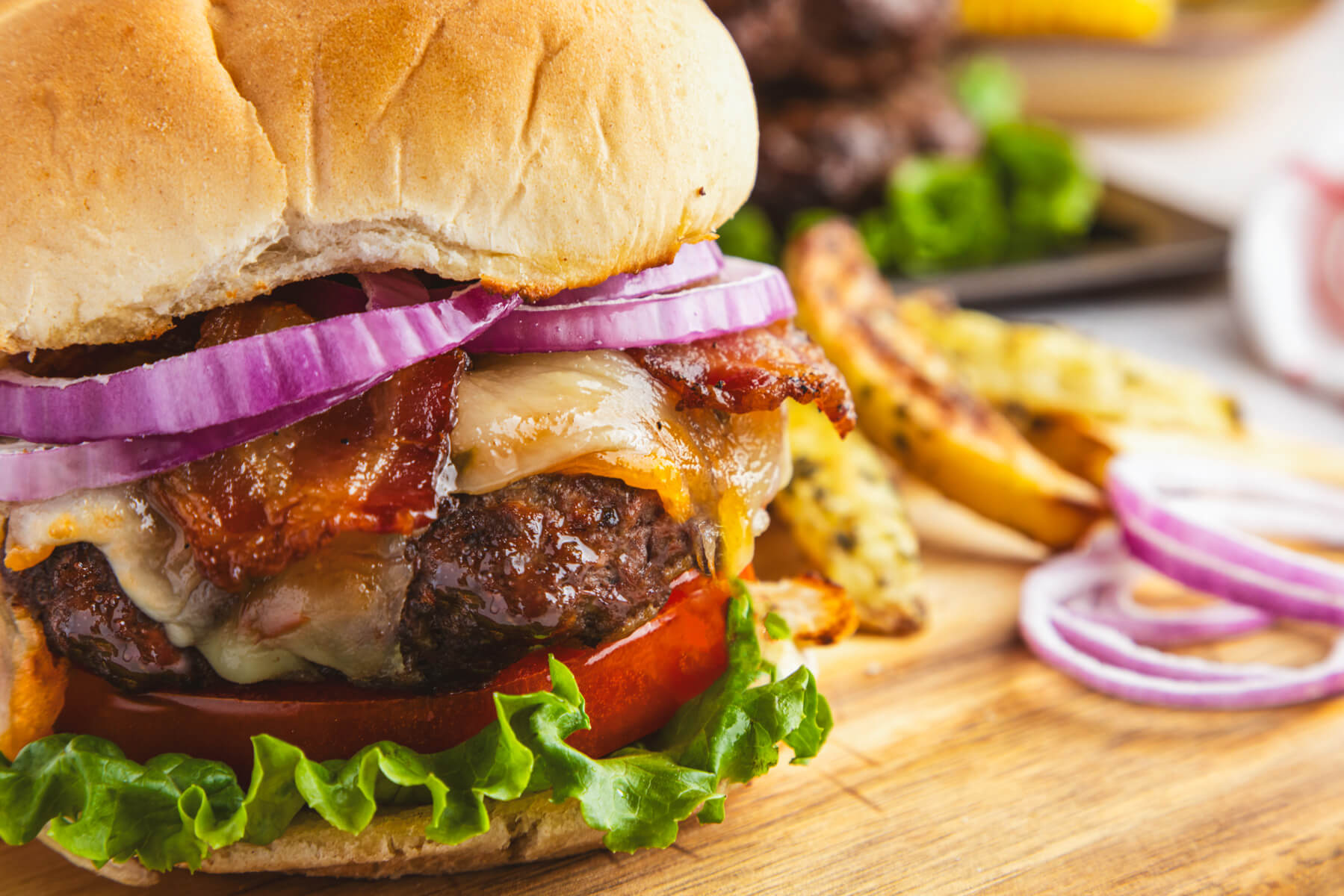 A juicy grilled Bison Burger in a bun with lettuce, tomatoes, cheese, bacon, and red onion slices with a side of truffle fries.