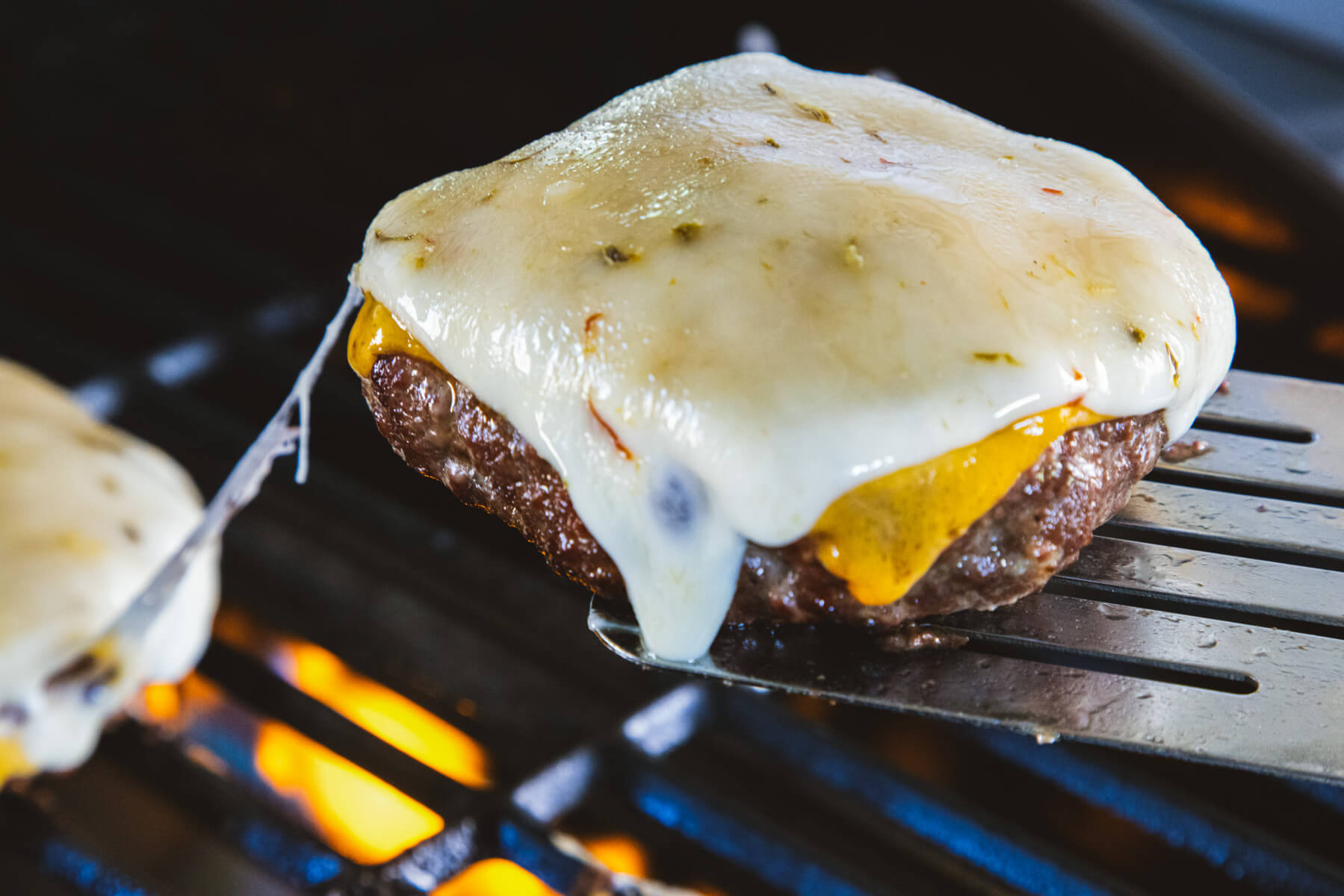 A juicy bison burger topped with melted cheese on a hot grill.