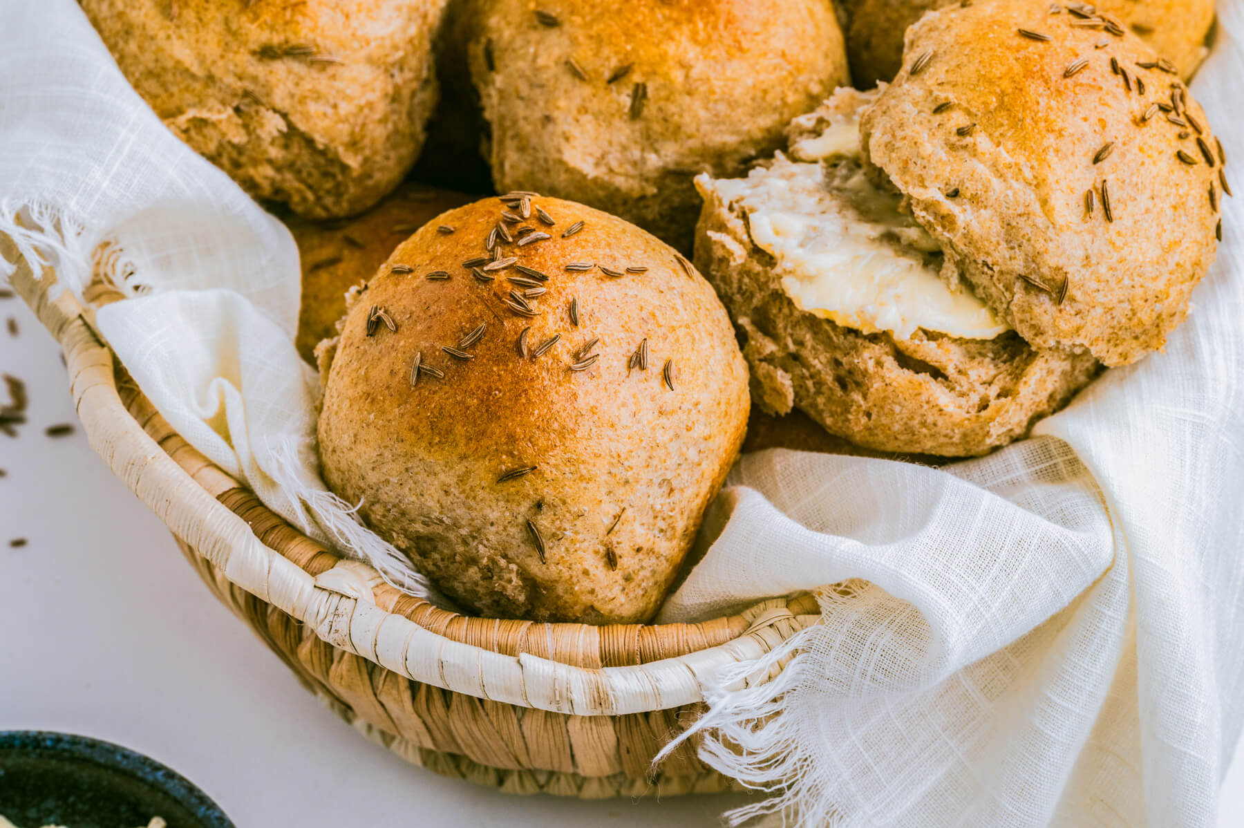 A basket filled with golden baked rye dinner rolls dotted with caraway seeds.