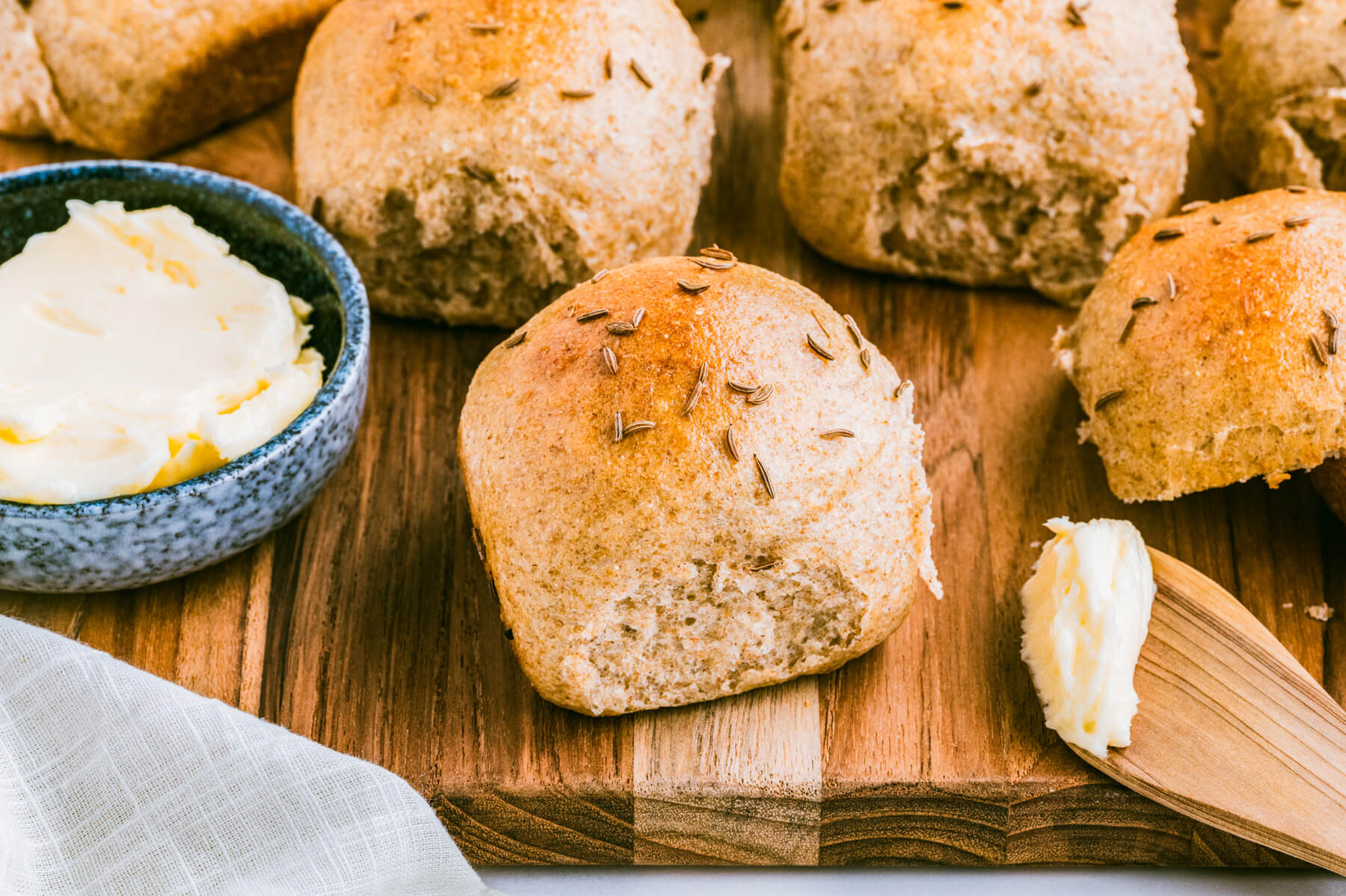 A group of golden baked rye dinner rolls dotted with caraway seeds on a wooden board.