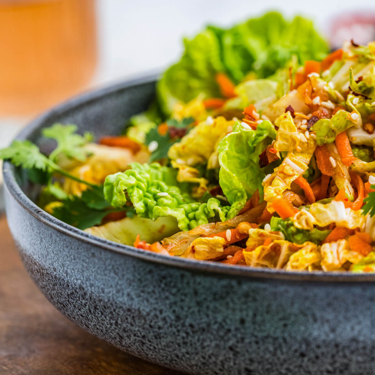 A bowl of vibrant kimchi slaw with green cilantro, sesame seeds, and shredded carrots on a wooden board.