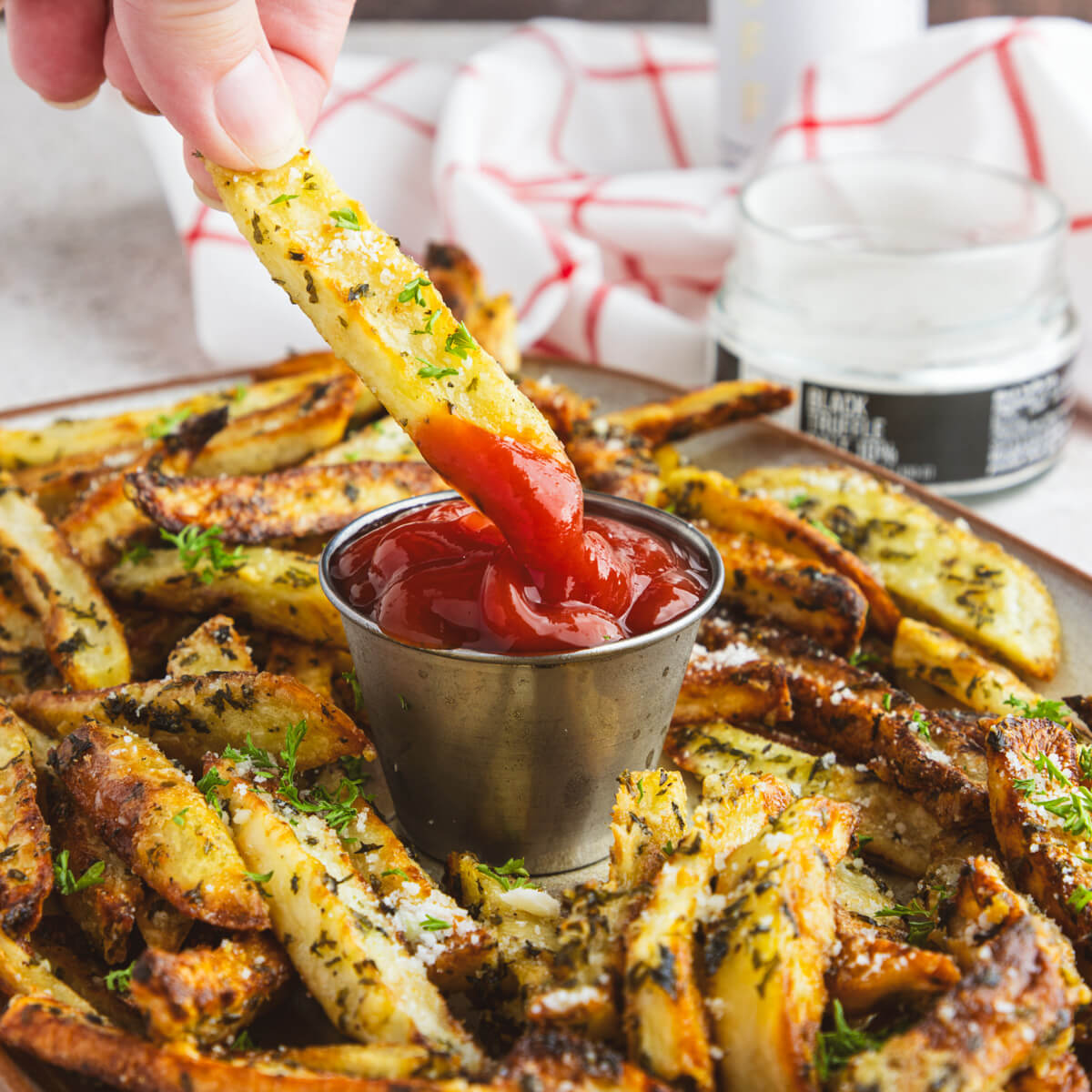 A hand dips a fry into a container of ketchup surrounded by oven baked truffle fries.