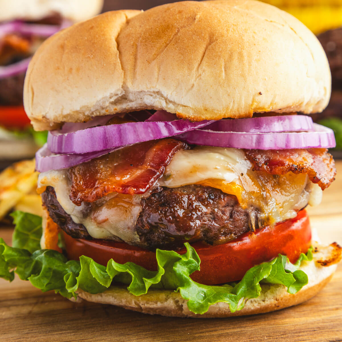 A juicy grilled Bison Burger in a bun with lettuce, tomatoes, cheese, bacon, and red onion slices.