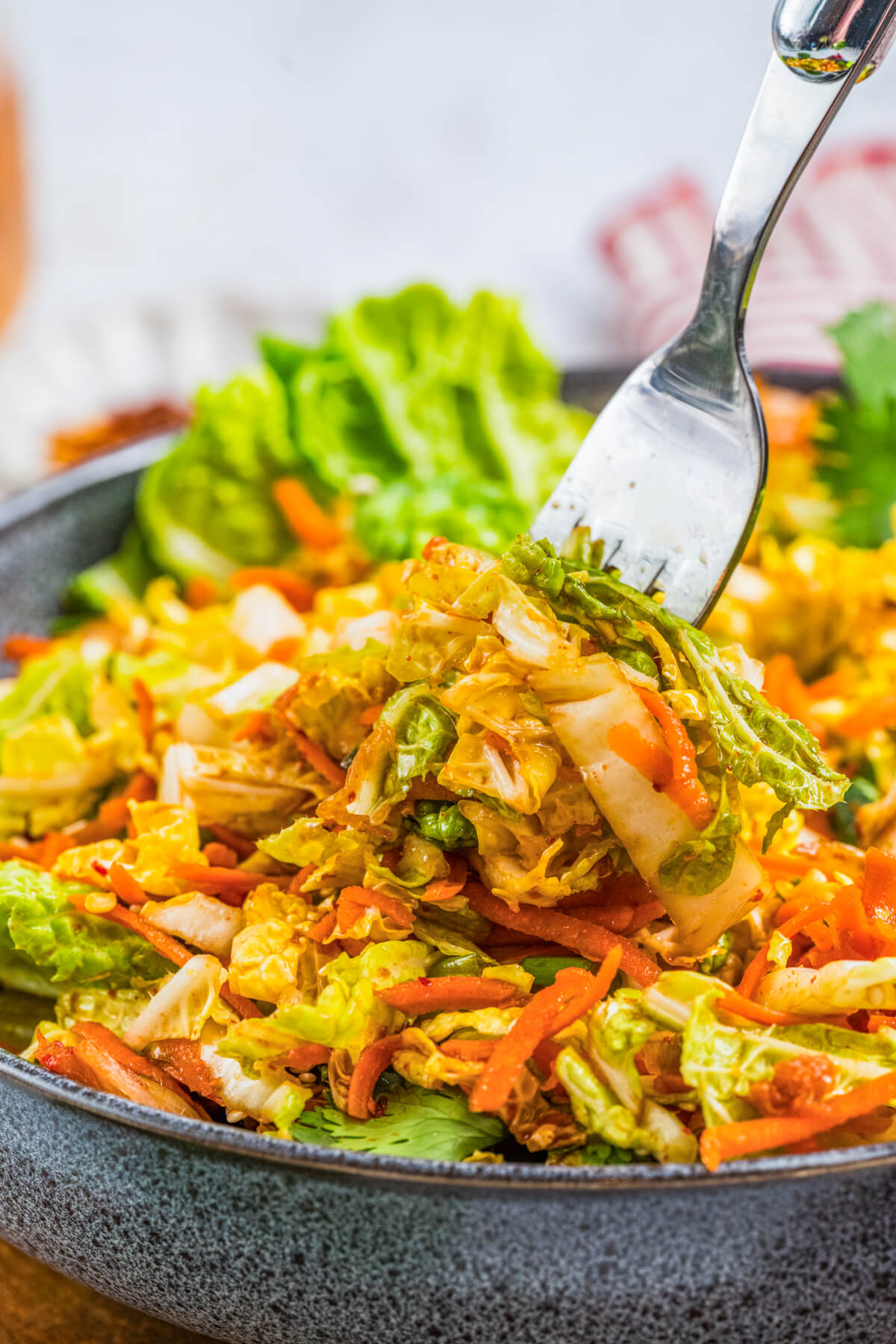 A fork taking a scoop of vibrant Kimchi Slaw from a large salad bowl.
