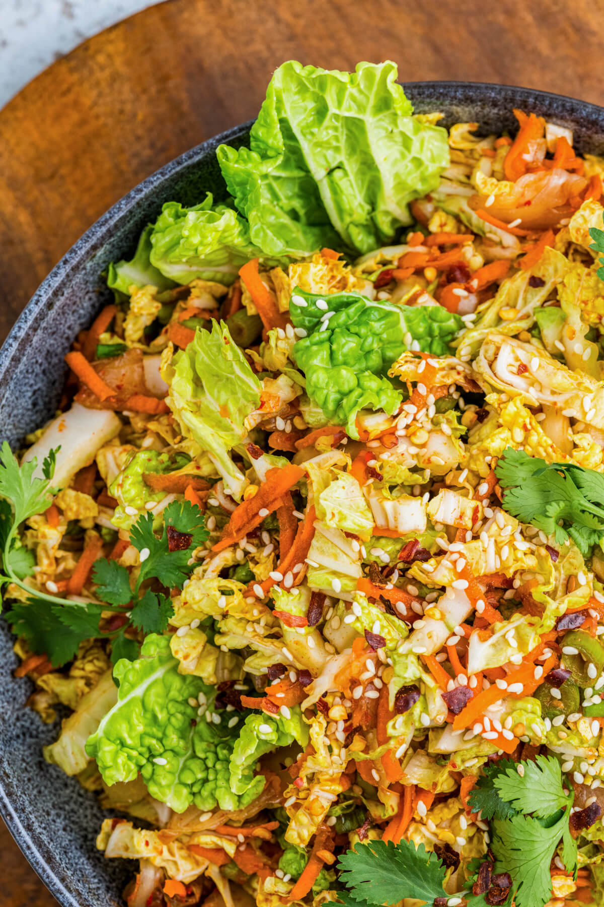A bowl of vibrant kimchi slaw with green cilantro, sesame seeds, and shredded carrots on a wooden board.