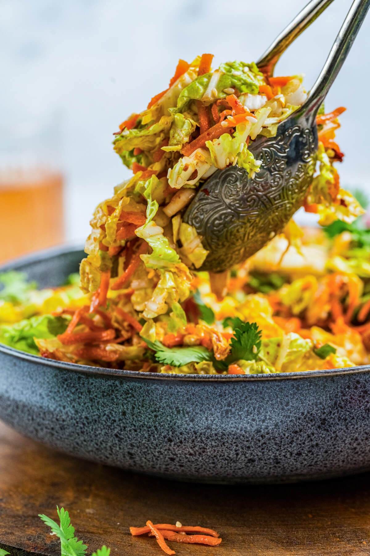 A pair of tongs taking a scoop of vibrant Kimchi Slaw from a large salad bowl.
