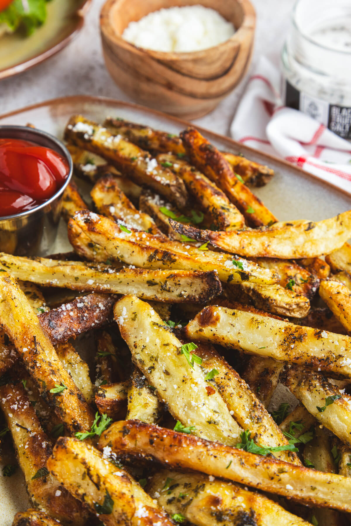 A plate of golden brown oven baked truffle fries dotted with parsley and black truffle salt with a container of ketchup.