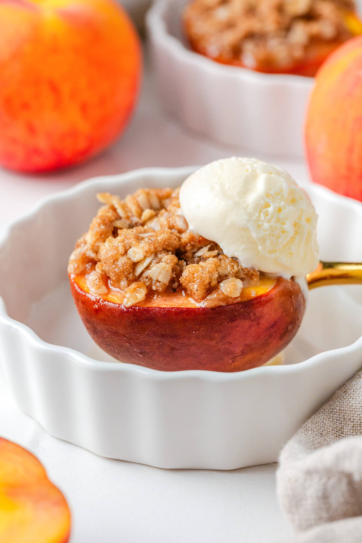One baked peach topped with golden brown buttery oat crumble and a scoop of vanilla ice cream in a serving dish.