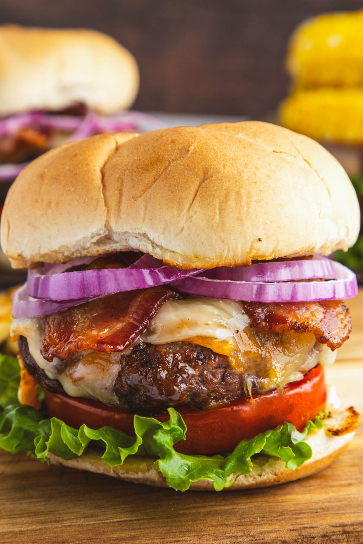A juicy grilled Bison Burger in a bun with lettuce, tomatoes, cheese, bacon, and red onion slices.