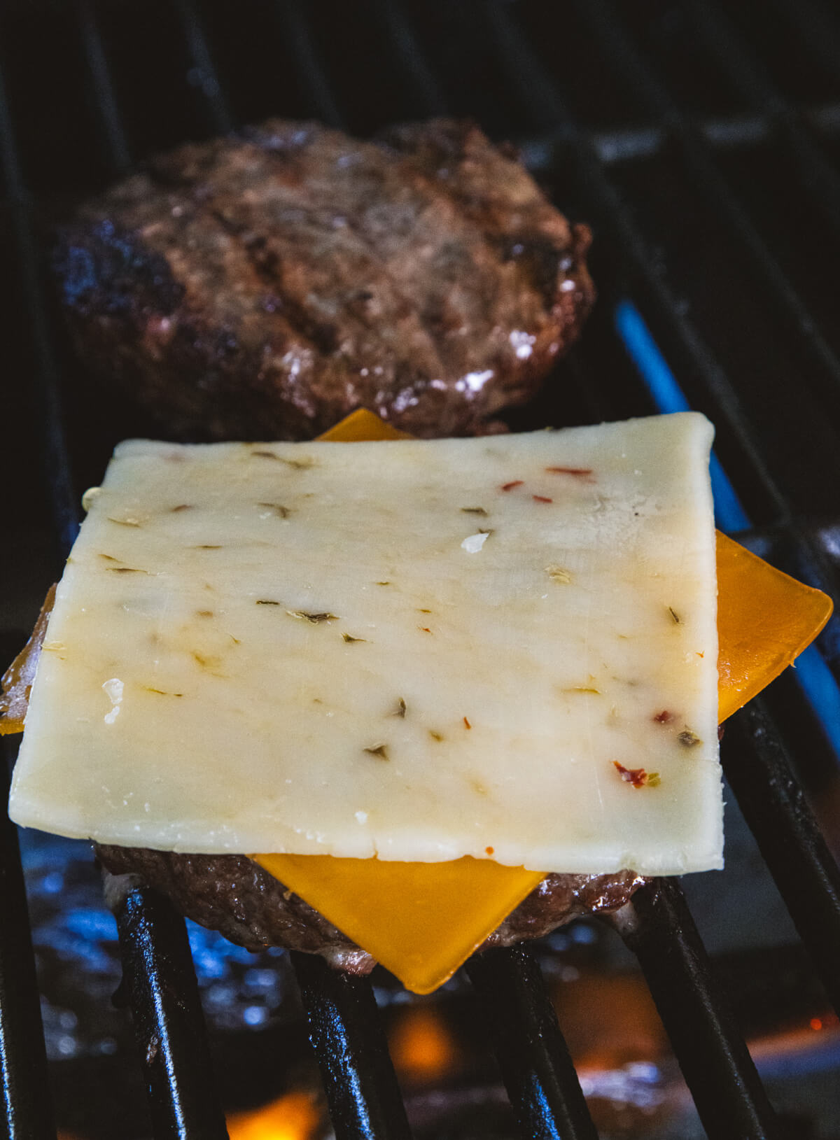 A juicy bison burger topped with two slices of cheese on a hot grill.