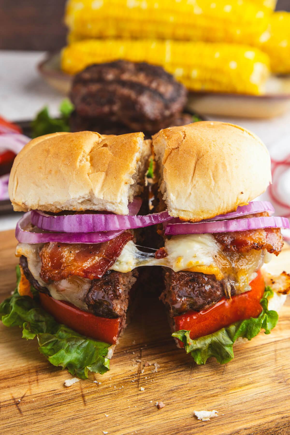 A juicy grilled Bison Burger in a bun with lettuce, tomatoes, cheese, bacon, and red onion slices sliced in half.