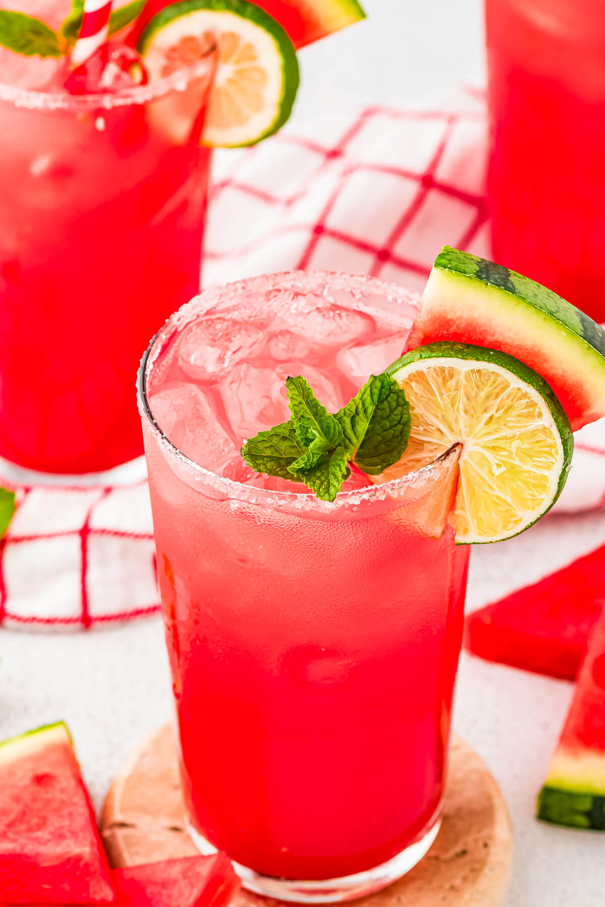 Two tall sugar rimmed glasses filled with vibrant watermelon agua fresca garnished with mint sprigs, lime wheels, and a small slice of watermelon.